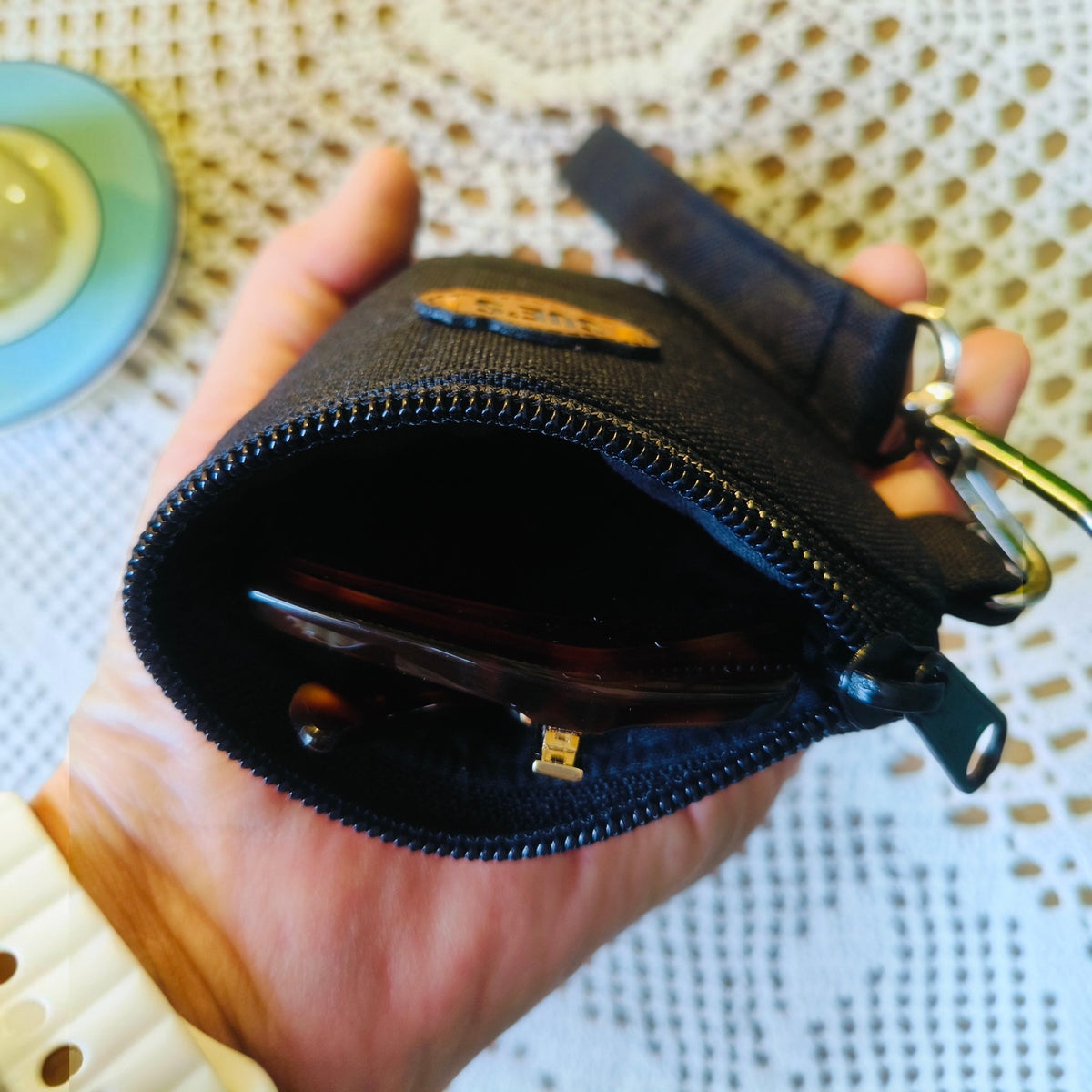 Suepatchwork black fabric glasses case with magnetic closure and wrist strap held in hand