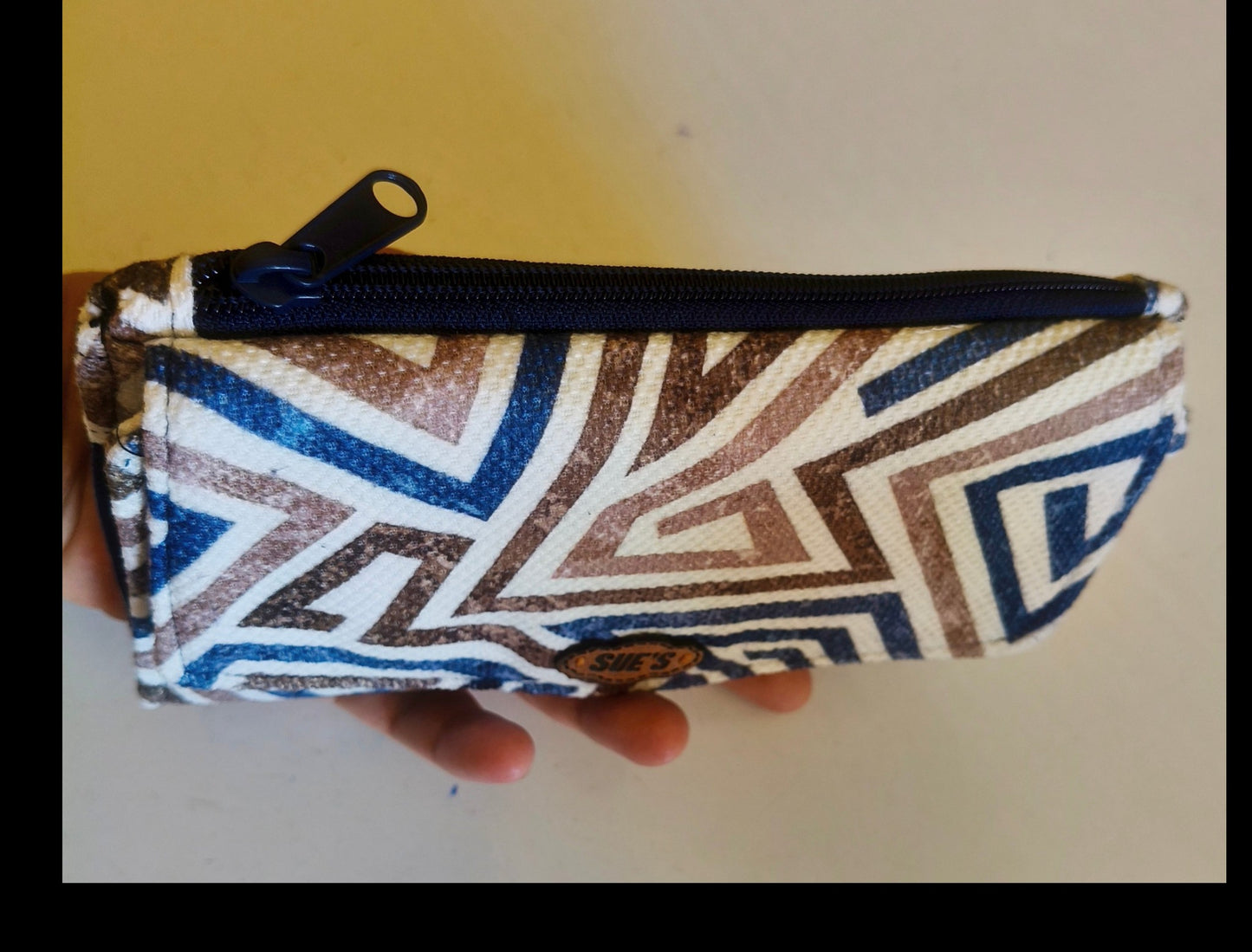 Suepatchwork blue and brown geometric print fabric trifold wallet with a secure zip closure held in a hand