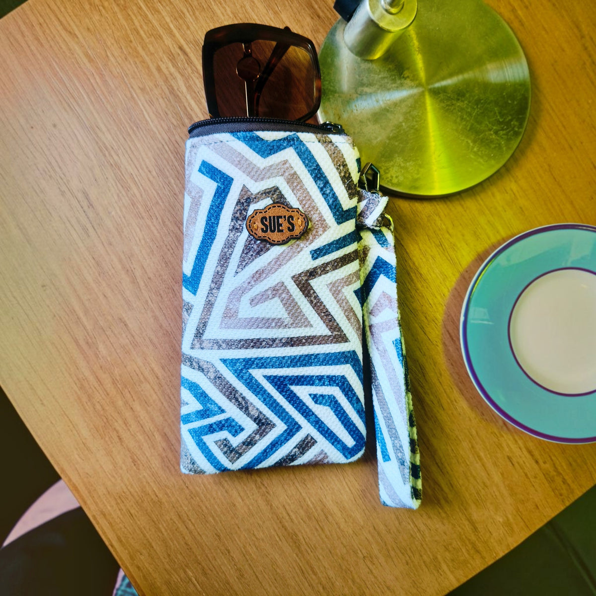 Suepatchwork blue geometric fabric glasses case with magnetic closure and wrist strap on a wooden table