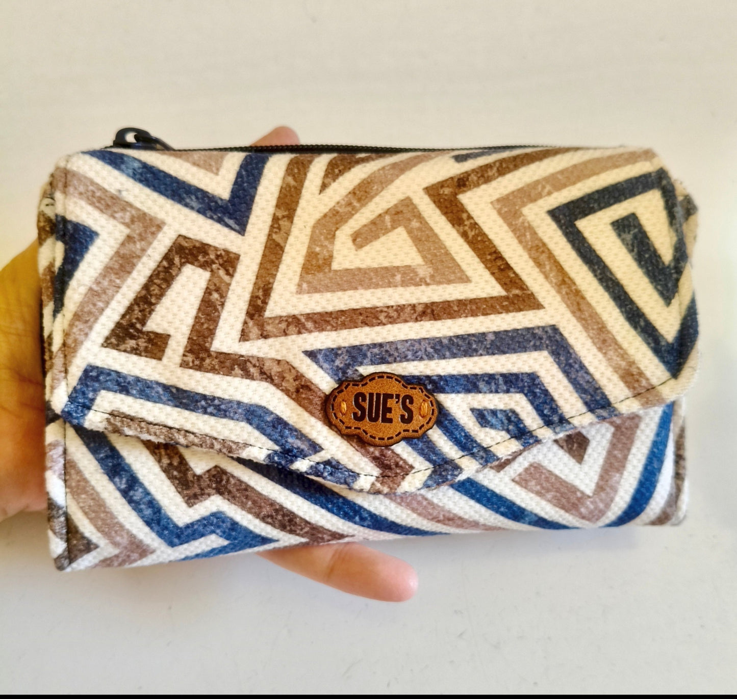 Suepatchwork blue and brown geometric print trifold fabric wallet with a leather logo tag held in a hand.