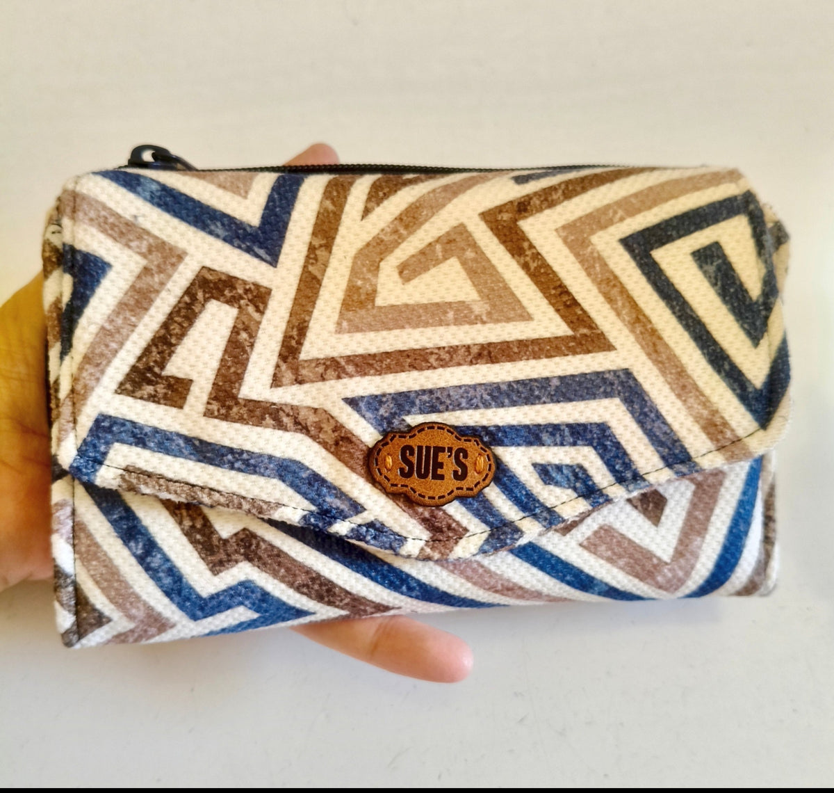Suepatchwork blue and brown geometric print trifold fabric wallet with a leather logo tag held in a hand.