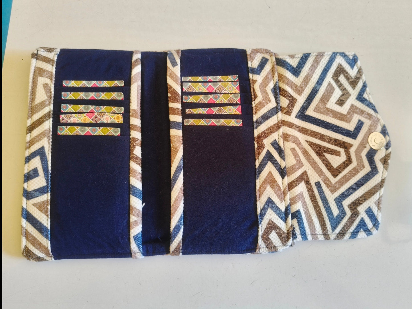 Suepatchwork blue trifold fabric wallet with geometric patterned accents, multiple card slots, and magnetic closure.