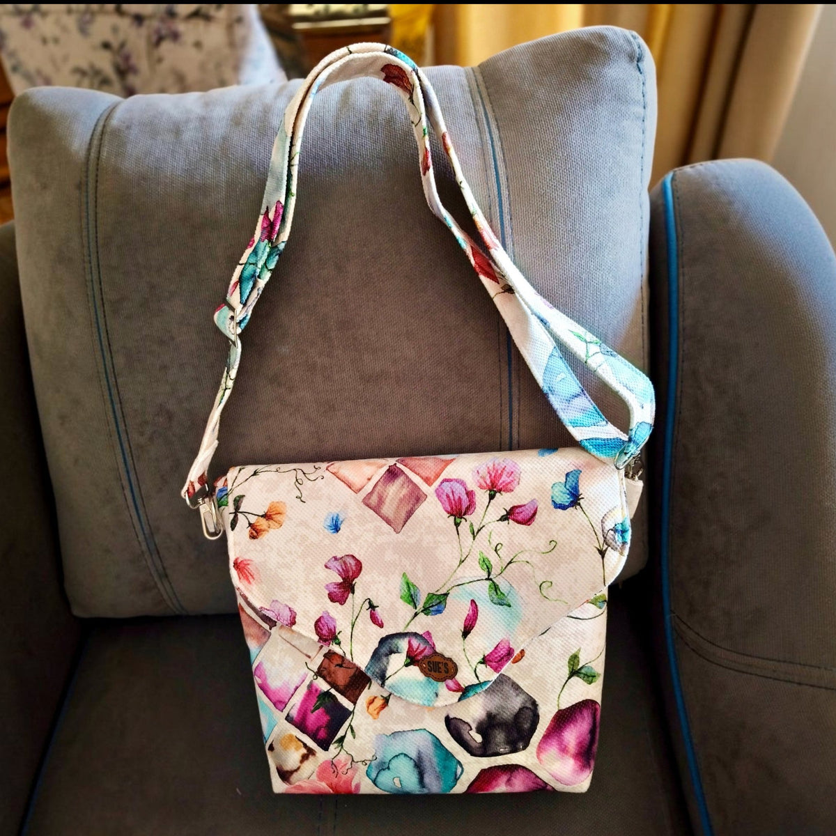 Suepatchwork handmade floral crossbody bag with adjustable strap, featuring a colourful flower pattern on fabric.