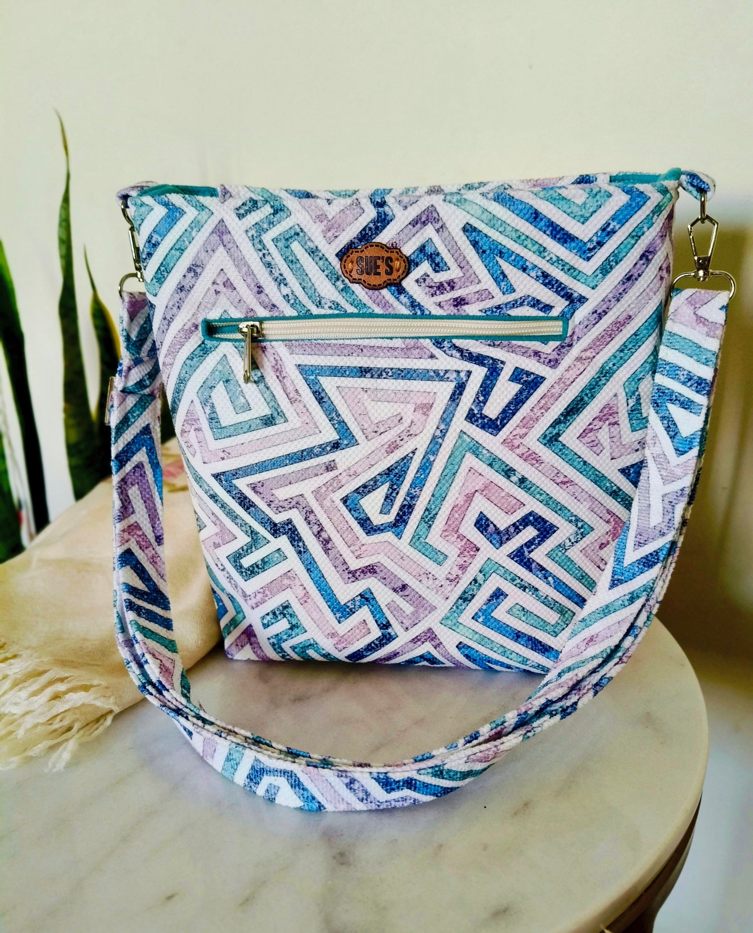 Suepatchwork crossbody bag with blue, purple, and white geometric maze pattern, featuring a front zipper and strap.