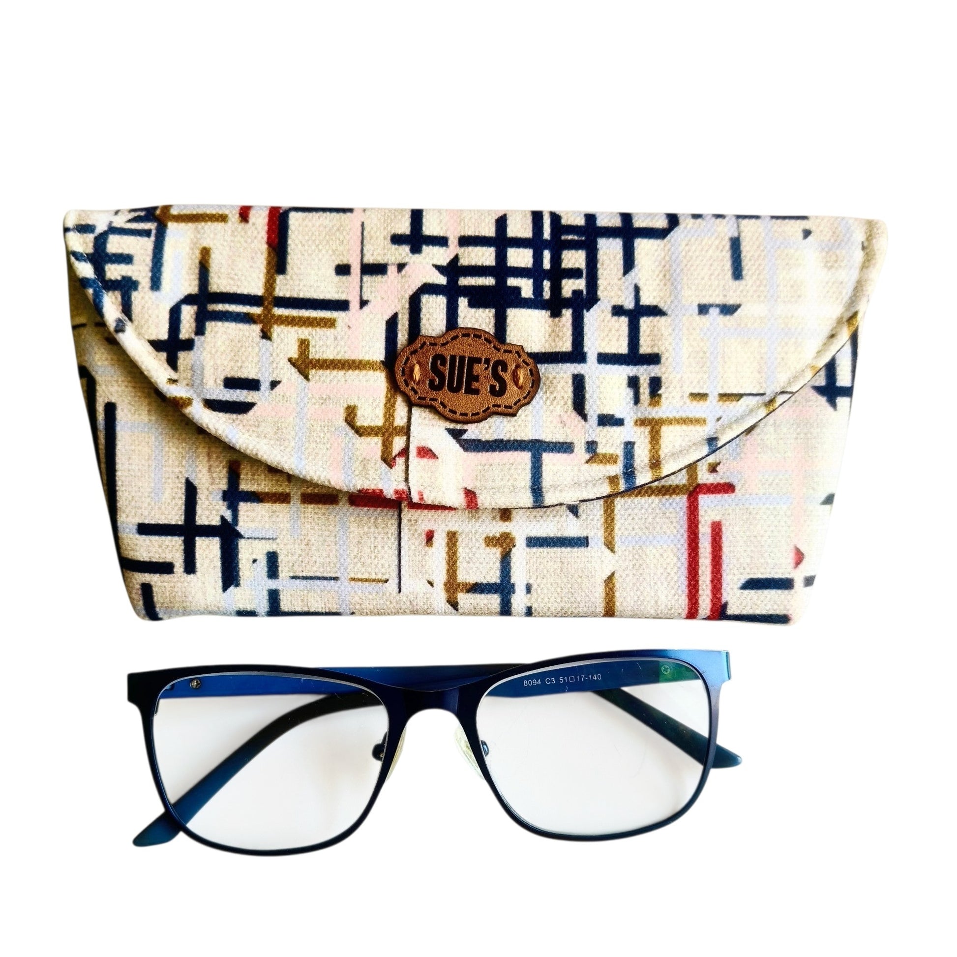 Suepatchwork handmade fabric glasses case with a geometric pattern and leather logo tag, shown with blue eyeglasses.