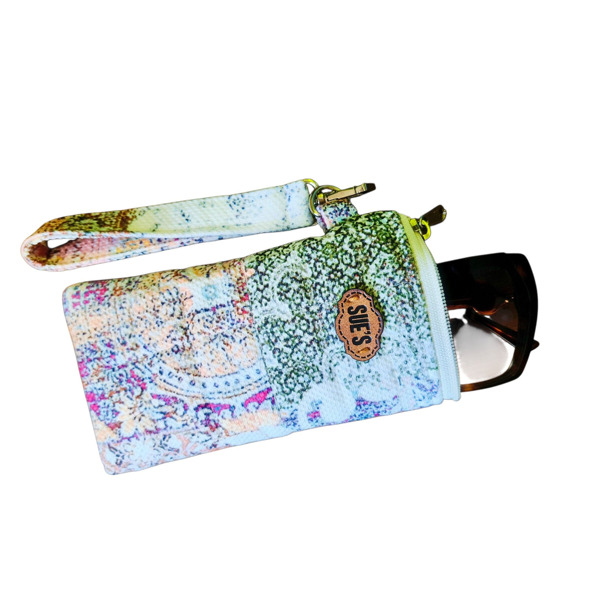 Suepatchwork handmade patchwork quilted long glasses case with a wrist strap and leather logo tag on a wooden table.