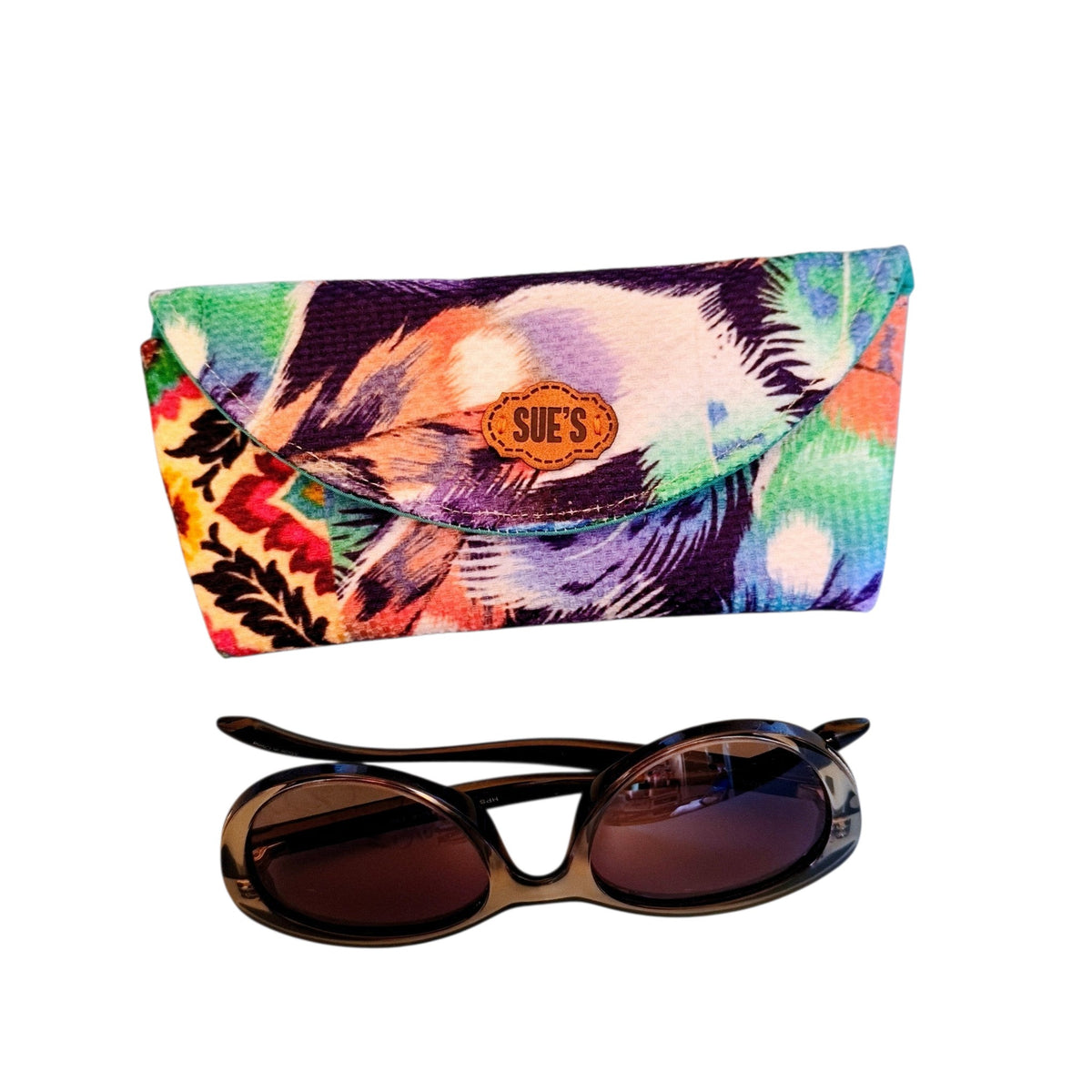 Suepatchwork handmade purple feather print fabric glasses case with a leather logo tag next to dark sunglasses